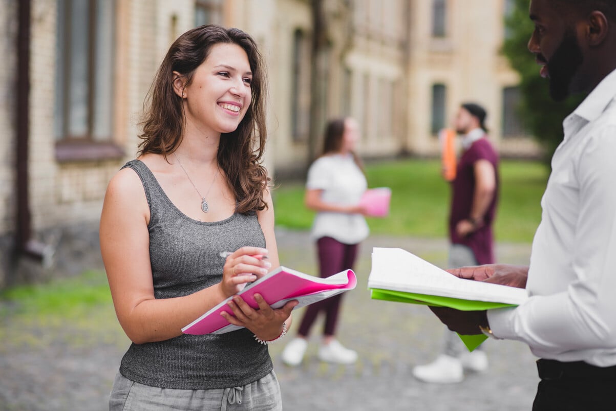 students-standing-outside-smiling-holding-notebooks